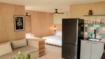 Una cocina compacta con refrigerador, una zona de comedor con mesa y sillas, y una cama al fondo.