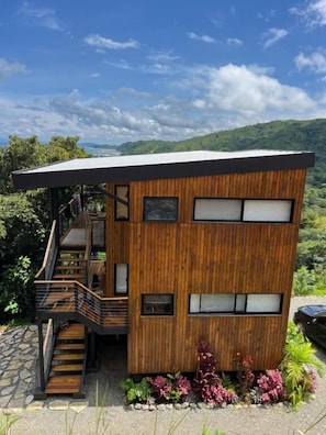 A modern two-story house with a wooden exterior, a staircase, and a view of the surrounding landscape.