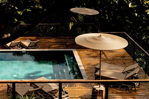 Una terraza de madera con piscina, sillas de descanso y un gran paraguas.