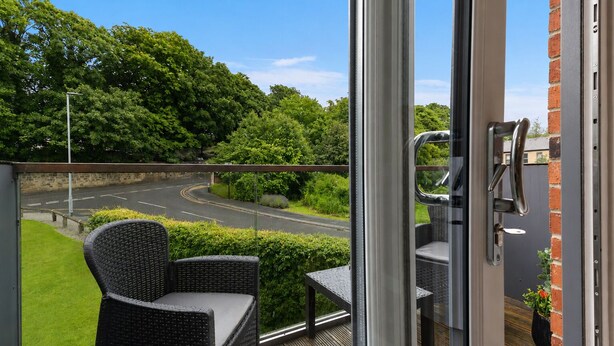 Een balkon met rieten meubilair, uitzicht op een weg en een bakstenen muur.