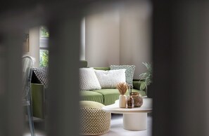 A room with a green sofa, white and patterned cushions, a round coffee table with decorative items, and a potted plant. - Finchdale Boutique Retreat (Wakefield)