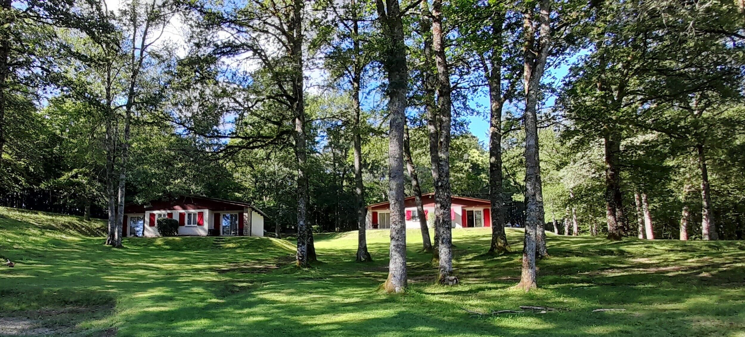 A red building surrounded by a forested area with a grassy foreground.
