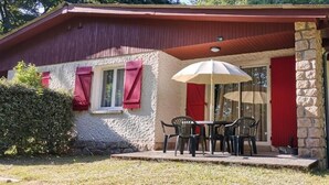 A house with a stone exterior, a red roof, and a covered patio with a table and chairs.