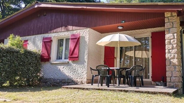 A house with a stone exterior, a red roof, and a covered patio with a table and chairs.