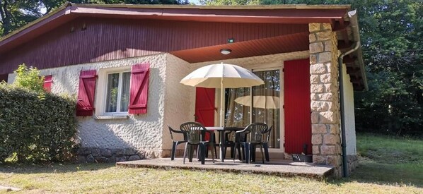 Une maison avec une façade en pierre, un toit rouge et un patio couvert avec une table et des chaises.