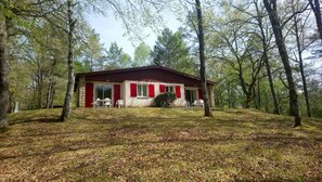 A single-story house with a red roof and white walls, surrounded by trees and a grassy area.