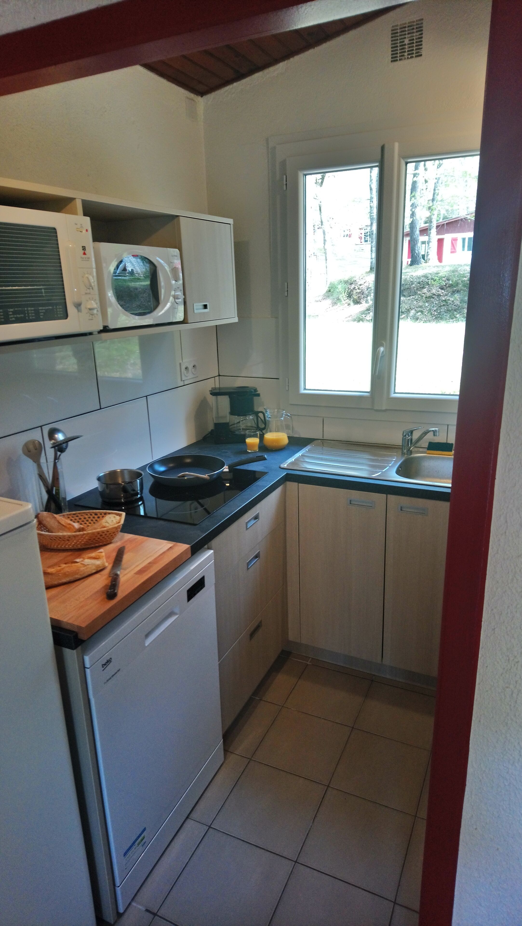 A compact kitchen with a microwave, stove, sink, and a window providing natural light.