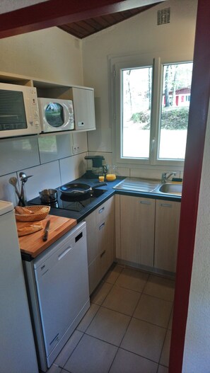 Cocina compacta con microondas, estufa, fregadero y ventana que proporciona luz natural.