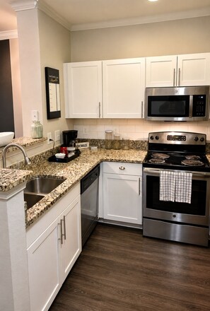 A kitchen with white cabinets, a stainless steel microwave, a stove, and a dishwasher.