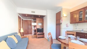 Een moderne woonkamer met een bank, tv-meubel, eettafel en keukenhoek.