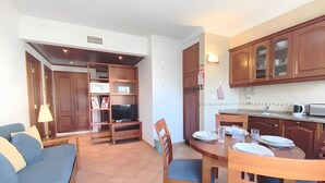 Een moderne keuken met houten kastjes, een eettafel gedekt voor vier personen, en een televisie in de woonkamer.