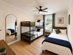 Un dormitorio con literas, una cama individual, un ventilador de techo, una ventana con cortinas, una mesita de noche pequeña y un espejo.