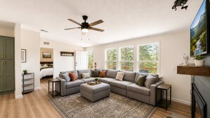 Ein Wohnzimmer mit Ecksofa, Deckenventilator, großem Fenster und Kamin.