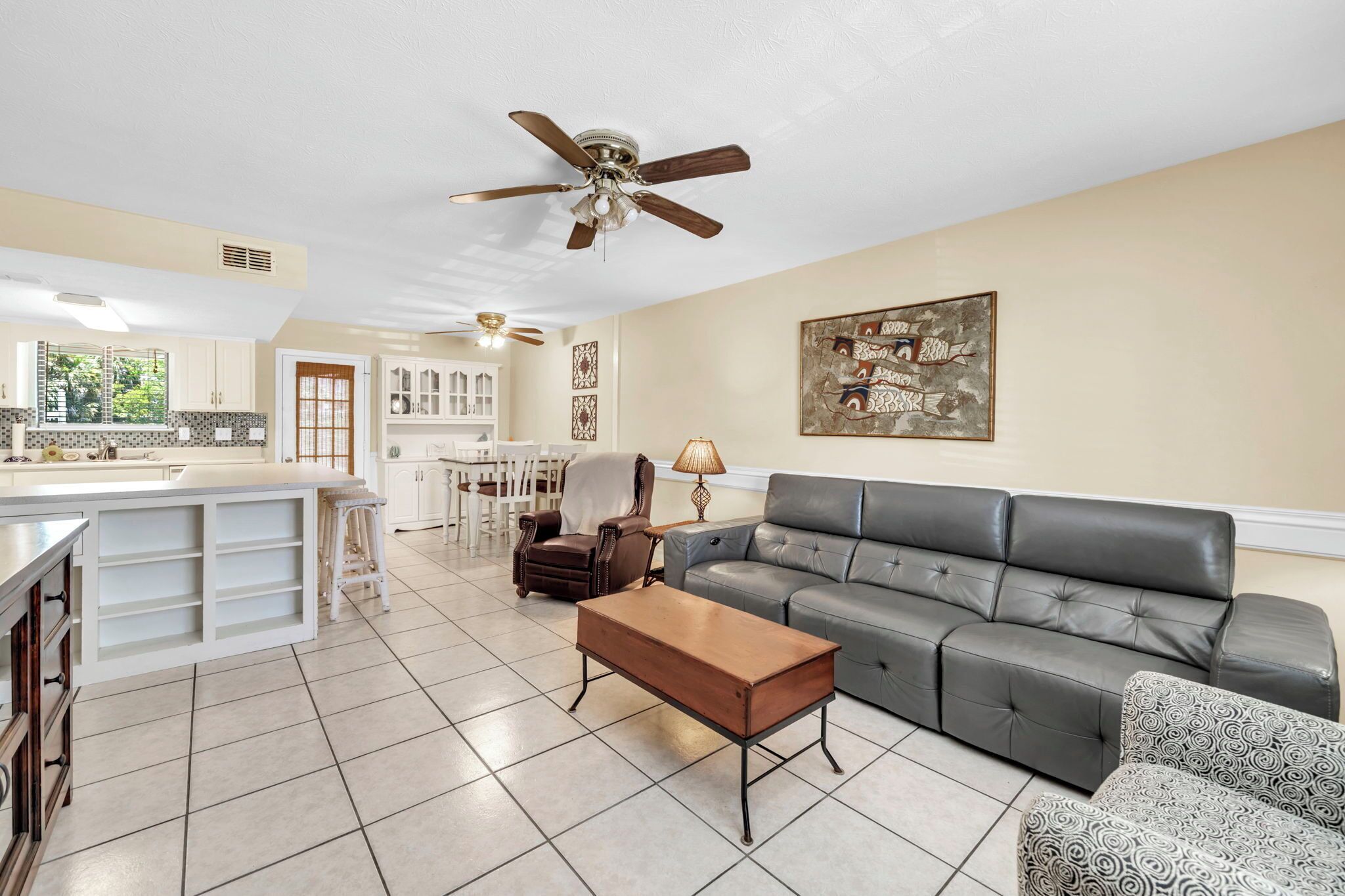 A spacious living area with a sofa, a coffee table, a ceiling fan, and a kitchen in the background.
