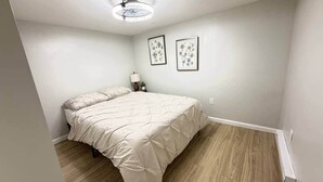 A bedroom with a bed, a nightstand, a lamp, and two framed pictures on the wall. - Historic Barn View | Cozy Ground Level Retreat (Frelinghuysen Township)
