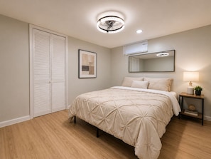 A bedroom with a bed, a bedside table with a lamp, a mirror, and a picture on the wall.