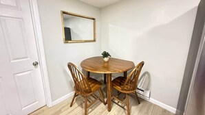A small dining area with a round wooden table and four chairs, a white door, and a wall-mounted mirror. - Historic Barn View | Cozy Ground Level Retreat (Frelinghuysen Township)