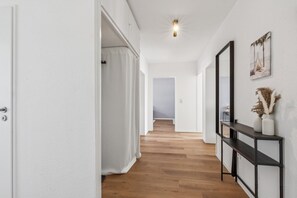 A hallway with wooden flooring, a white door, a black console table with a vase, and a framed picture on the wall. - Modern 90-square-meter apartment | 3 bedrooms | Balcony | Near Phantasialand (Wesseling)