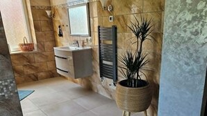 Ein Badezimmer mit Steinwand, Waschbecken, Spiegel, Handtuchhalter und einer Topfpflanze.