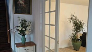 Ein Flur mit einer Holztreppe, einer weißen Tür mit Glasfenstern, einer Vase mit Blumen und einem Topfpflanzen.