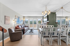 Ein modernes Wohnzimmer mit einer Couch, Sesseln, einem Esstisch und einem Fernseher.