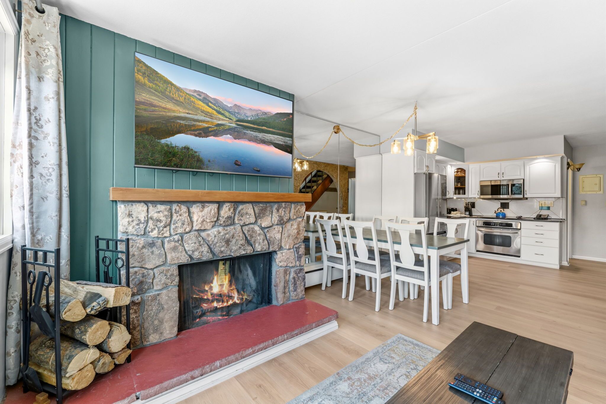 A living room with a stone fireplace, dining area, kitchen, and a large landscape painting.