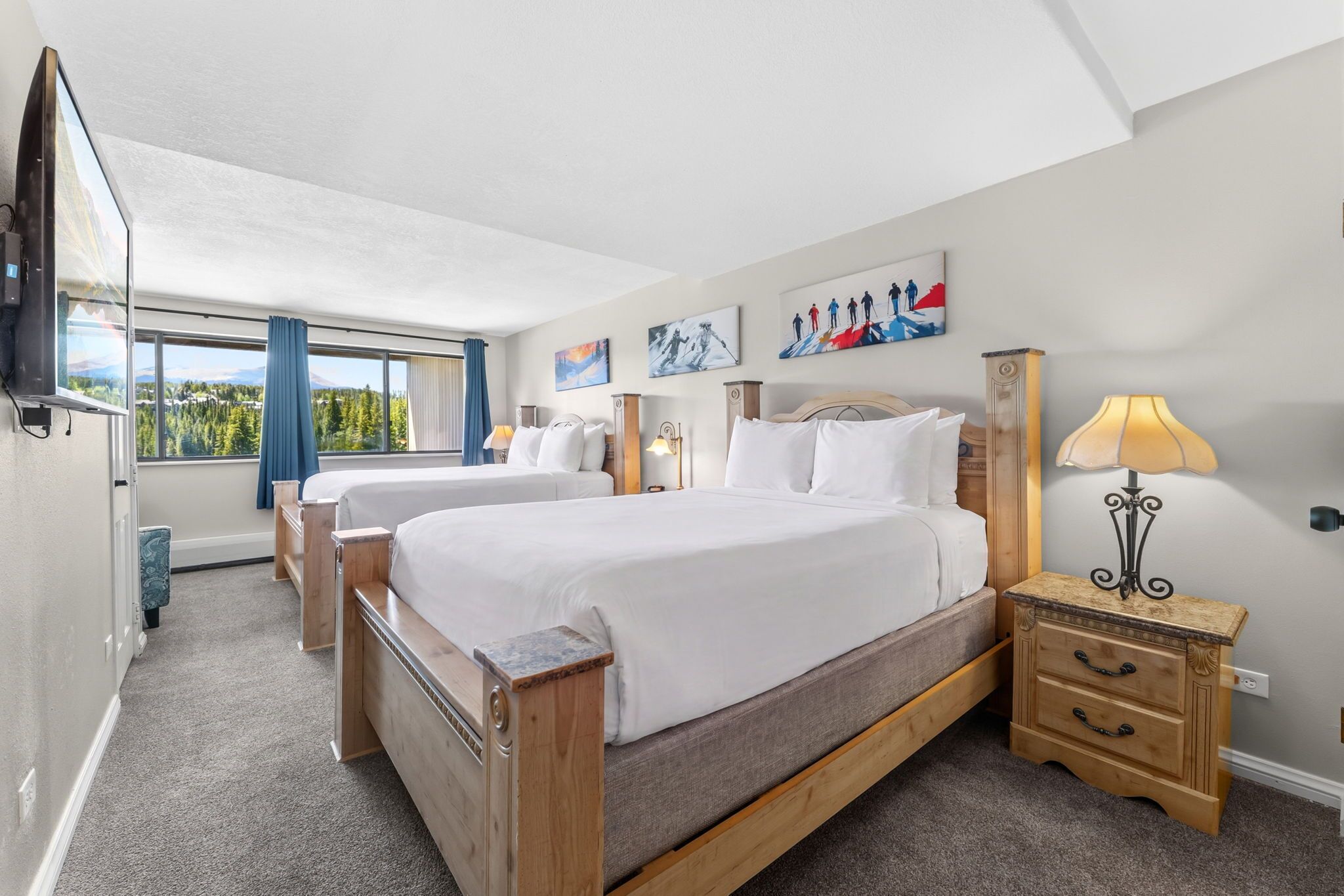 Ein Hotelzimmer mit zwei Betten, einem Fernseher, einer Lampe und Kunstwerken an den Wänden.