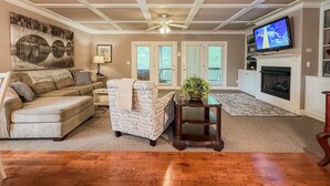 A living room with a sofa, armchair, TV, fireplace, and a ceiling fan. - Helen Riverfront Escape | Walk to Downtown (Helen)