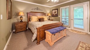 A bedroom with a bed, two bedside tables, a ceiling fan, a bench, a door with a view, and a framed picture on the wall. - Helen Riverfront Escape | Walk to Downtown (Helen)