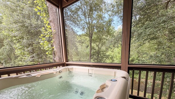 A hot tub with a wooden deck and a view of a forest. - Helen Riverfront Escape | Walk to Downtown (Helen)