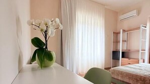 Hotellihuone, jossa on sänky, työpöytä, tuoli, ikkuna verhoilla ja ilmastointilaite.