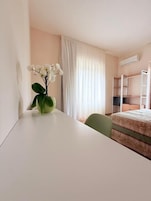 Una habitación de hotel con cama, escritorio, silla, ventana con cortinas y equipo de aire acondicionado.