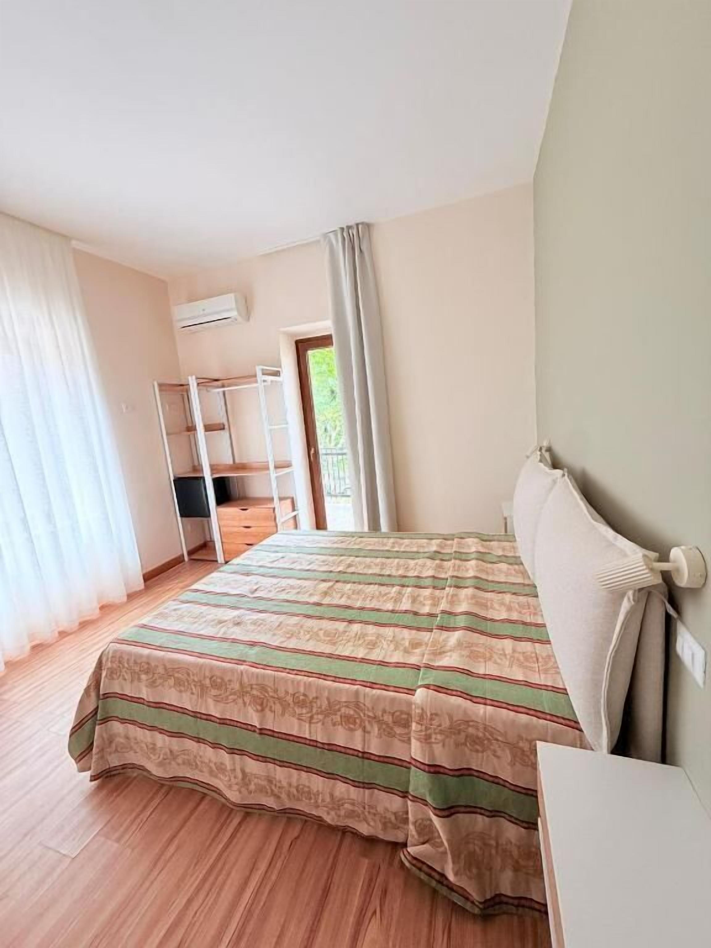 A bedroom with a bed, a desk, a wardrobe, and a window with curtains.