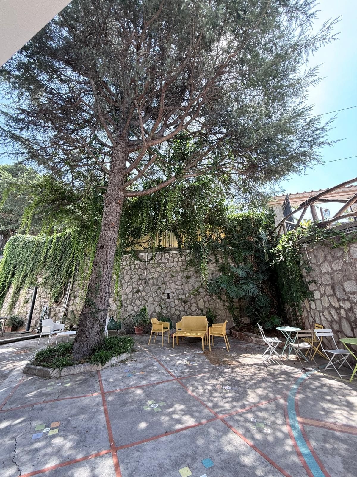 A courtyard with a large tree, stone wall, and outdoor seating area.
