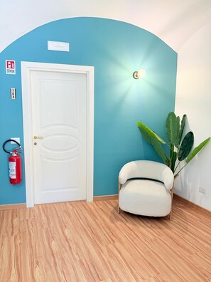 A room with a white door, a fire extinguisher, a potted plant, and a light fixture on the wall.