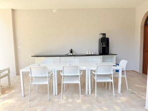 A dining area with a white table and chairs, a coffee machine, and a small kitchen area.