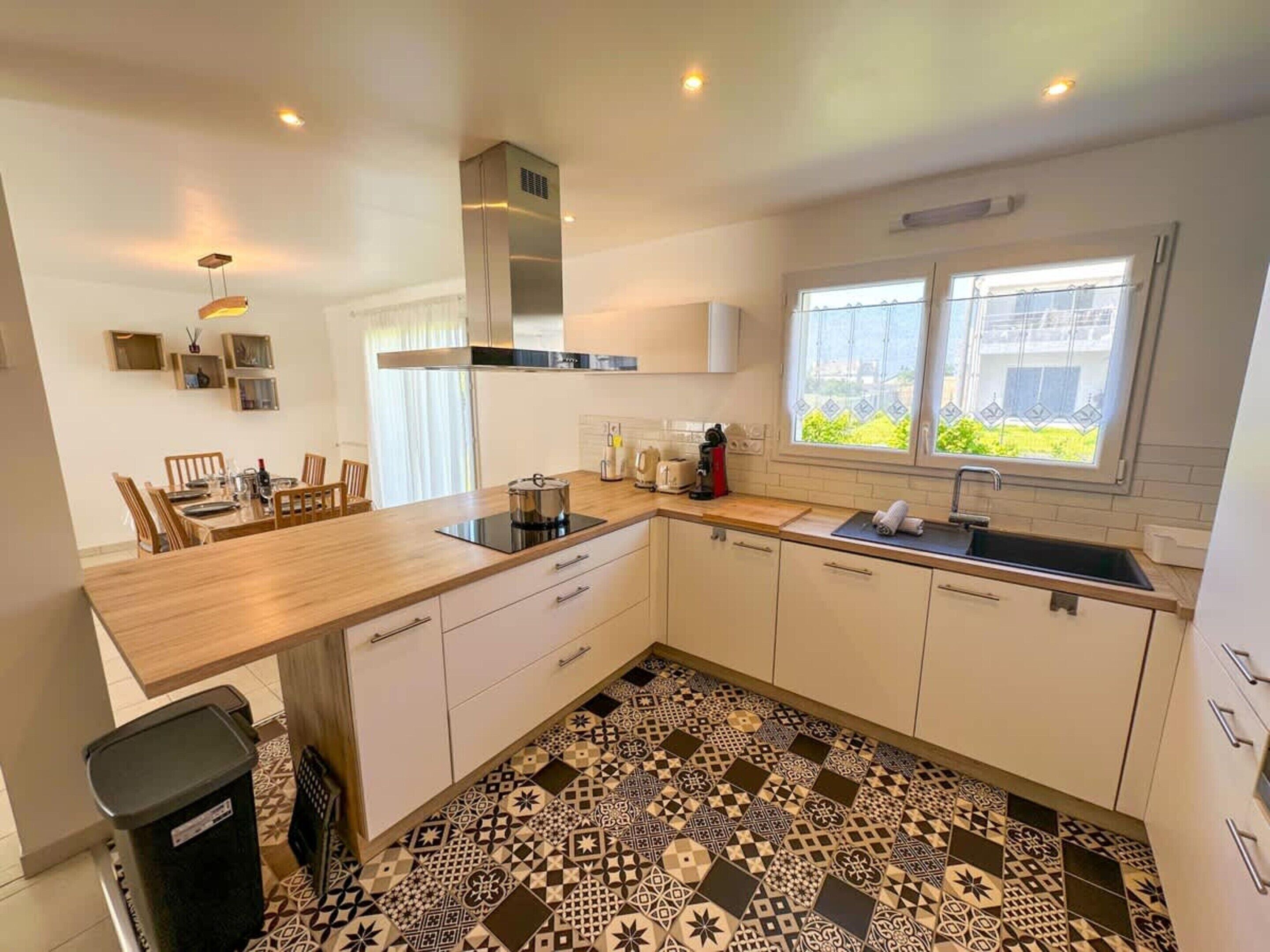 A modern kitchen with a dining area, a large window, and patterned flooring.