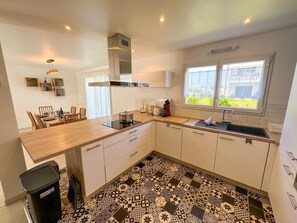 A modern kitchen with a dining area, a large window, and patterned flooring. - 3BR Coastal Home With Garden & Terrace (Plouguerneau)