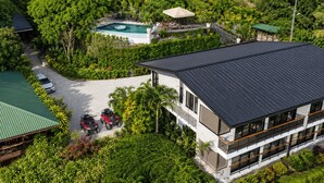 En moderne bygning med to etager og en swimmingpool, omgivet af frodigt grønt.