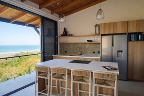 A modern kitchen with a large island, wooden cabinets, and a view of the ocean. - Vista Naranja Luxury Villa - Santa Teresa (Santa Teresa)
