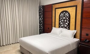 Une chambre d’hôtel avec un grand lit, une tête de lit en bois, une table de chevet avec un téléphone et un rideau.