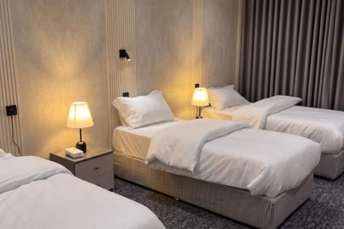 Habitació d'hotel amb tres llits, cadascun amb roba de llit blanca i vàries làmpades.
