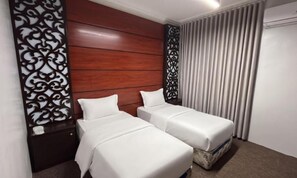 Une chambre d’hôtel avec deux lits simples, une tête de lit en bois, un panneau décoratif mural, une fenêtre avec des rideaux et un mur blanc.