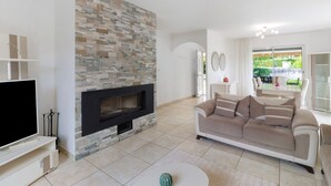 A living room with a stone fireplace, a beige sofa, and a flat-screen TV on a white stand. - Périgord House: Private Terrace, Wi-Fi & Air Conditioning (Pazayac)