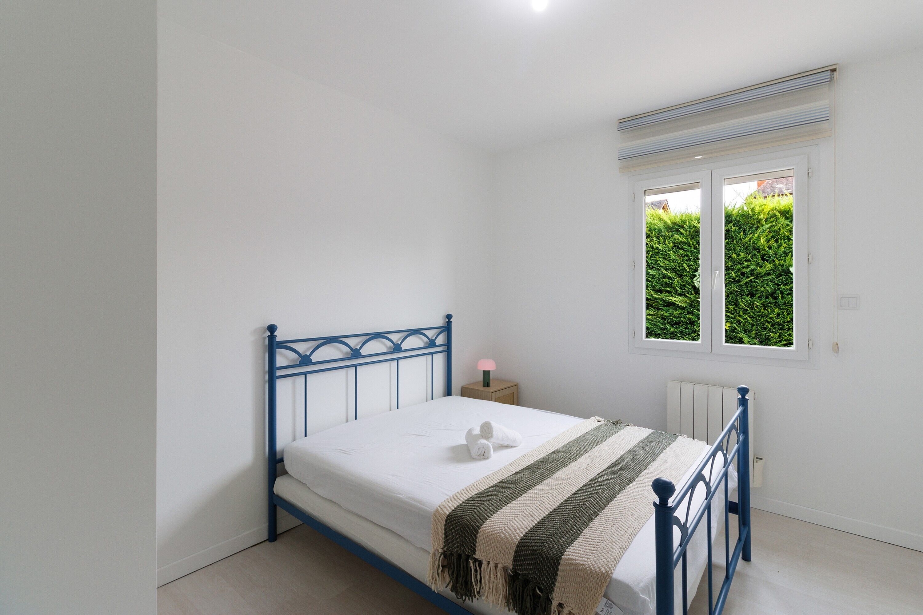 Een slaapkamer met een enkel bed, nachtkastje, raam en radiator.