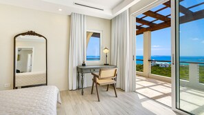 Ein Schlafzimmer mit Bett, Schreibtisch mit Stuhl, Spiegel und Meerblick vom Balkon.