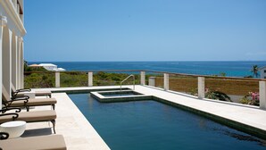 Ein Pool mit Blick auf den Ozean, Liegestühle und eine Holzterrasse.
