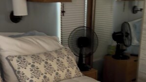 A bed with a quilted cover, a bedside fan, and wooden cabinets above. - Cozy 1-bd, Yuma, Winter Getaways, Dentacation. Private, Secure, Gated Community. (Yuma)