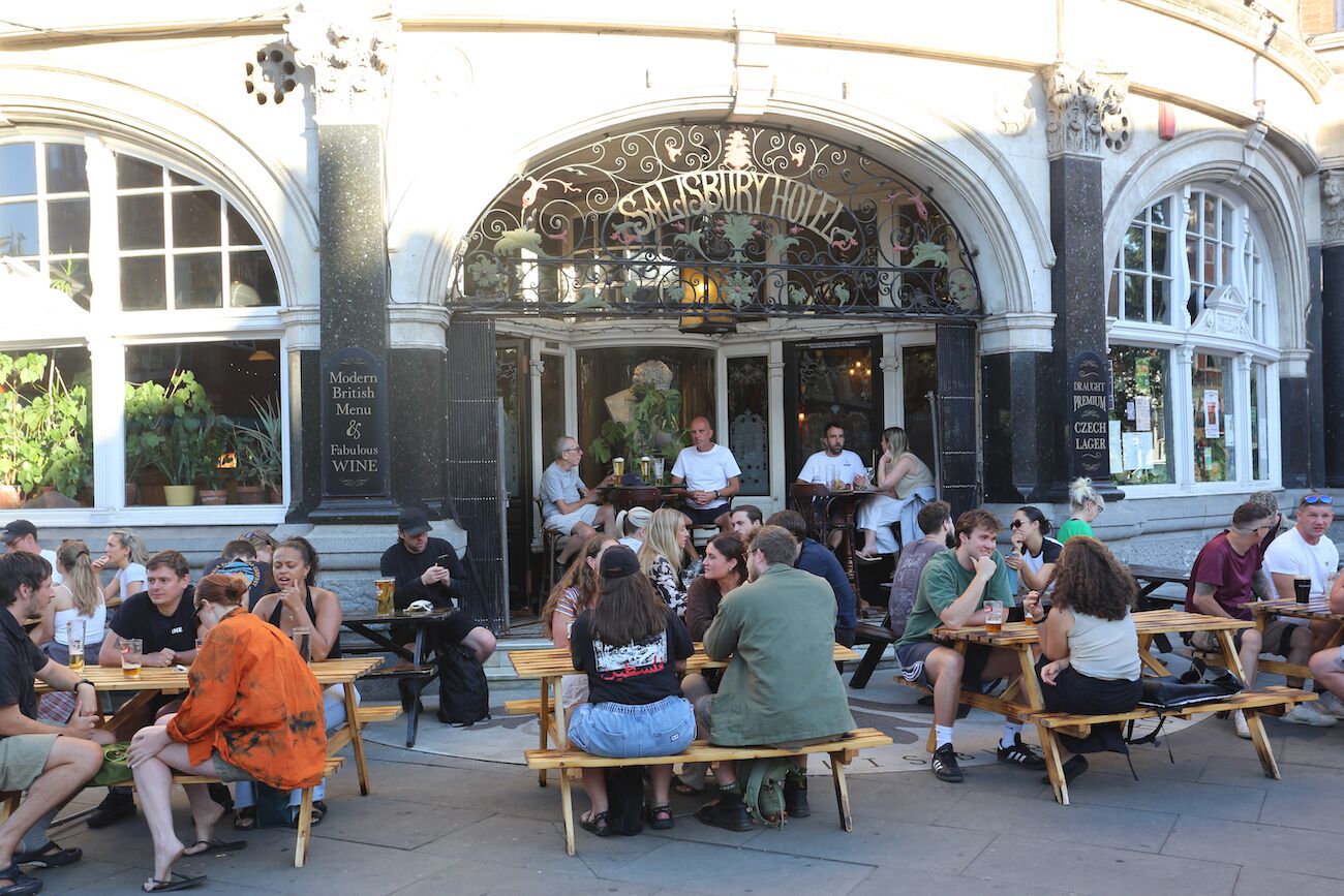An outdoor seating area with wooden tables and benches in front of a building with an arched entrance and a sign that reads 'Salisbury Hotel.' - Stunning house and garden - the perfect London base for your family vacation (London)