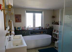 Ein Badezimmer mit einer freistehenden Badewanne, einem großen Fenster und einem Waschtisch mit Spiegel.